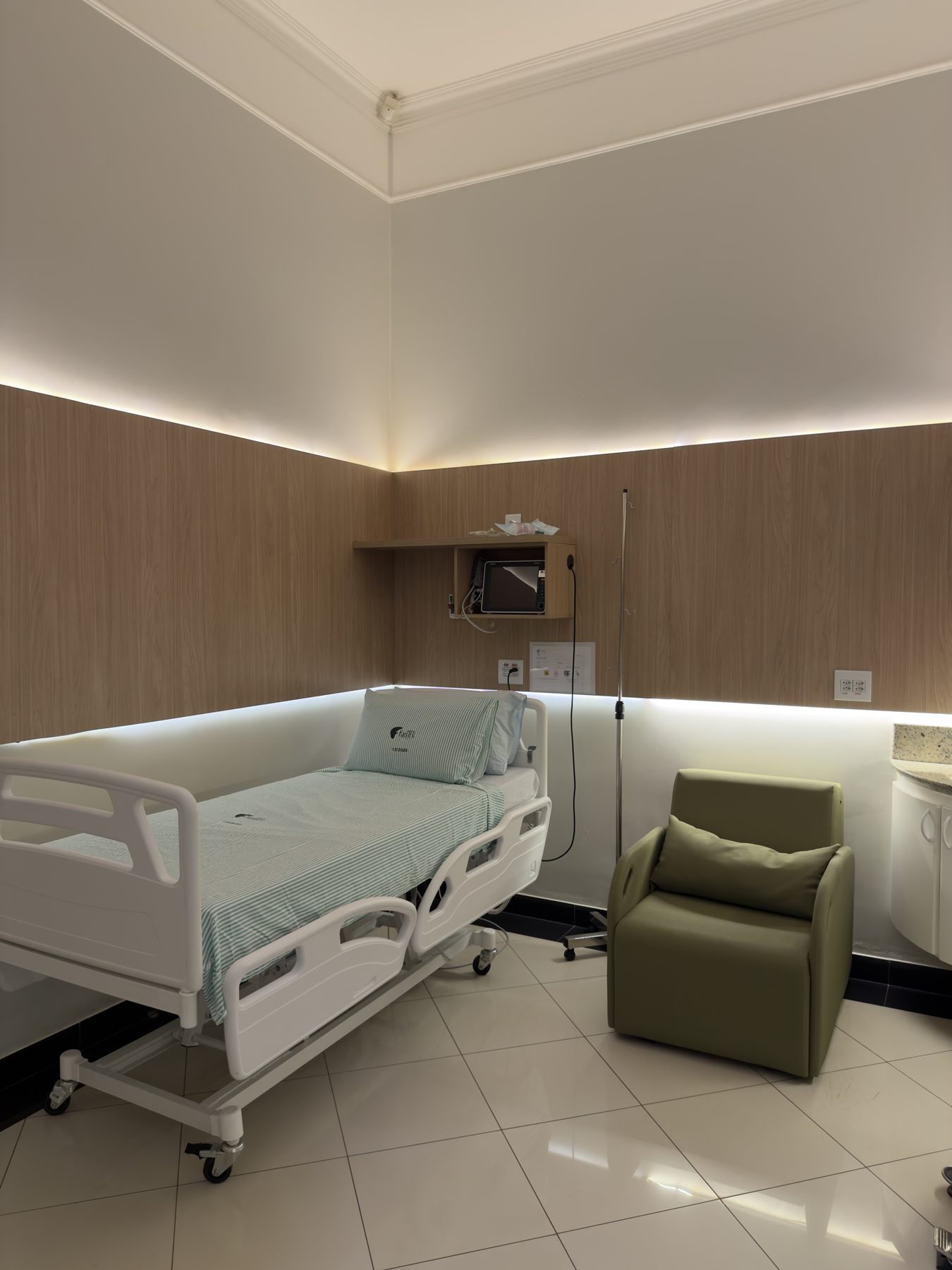 Suíte do Hospital Fases com cama hospitalar, poltrona e iluminação indireta